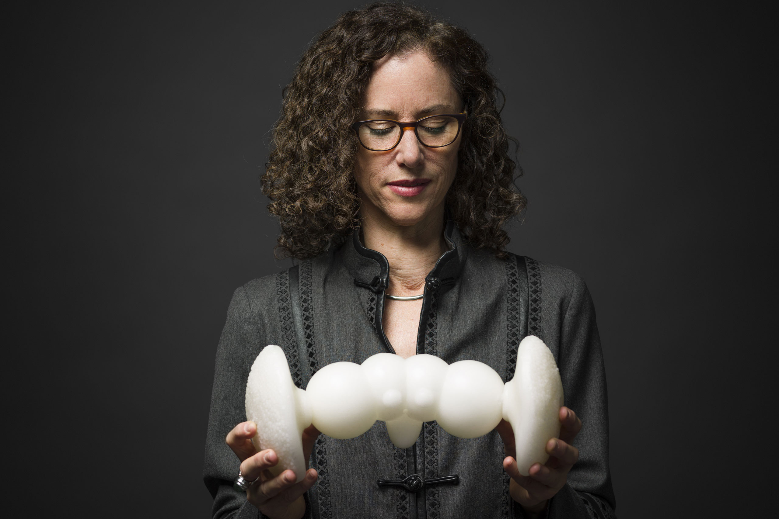 The artist Helen Pynor, wearing a dark shirt, glances down to a model of the visual circuit (visual nervous system) in the fruit fly Drosophila melanogaster, she holds with both hands. Helen made the model whilst in residence in the laboratory of neuroscientist Dr Iris Salecker at the Francis Crick Institute, London.
