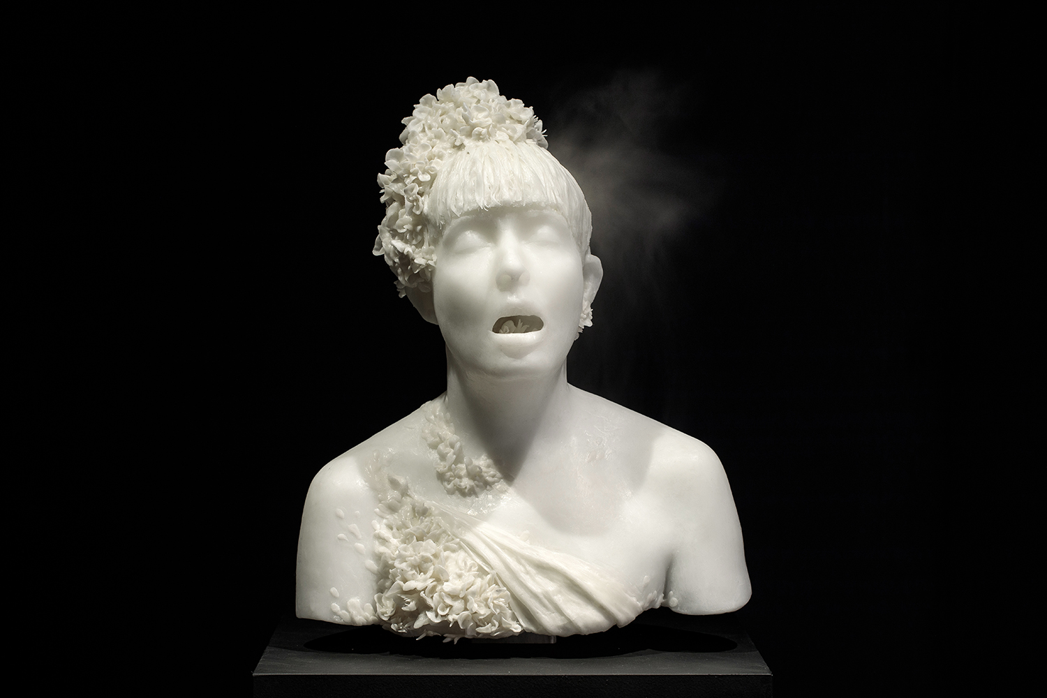 Set against a black background, the white sculpted bust of a woman exhales a plume of vapour.
