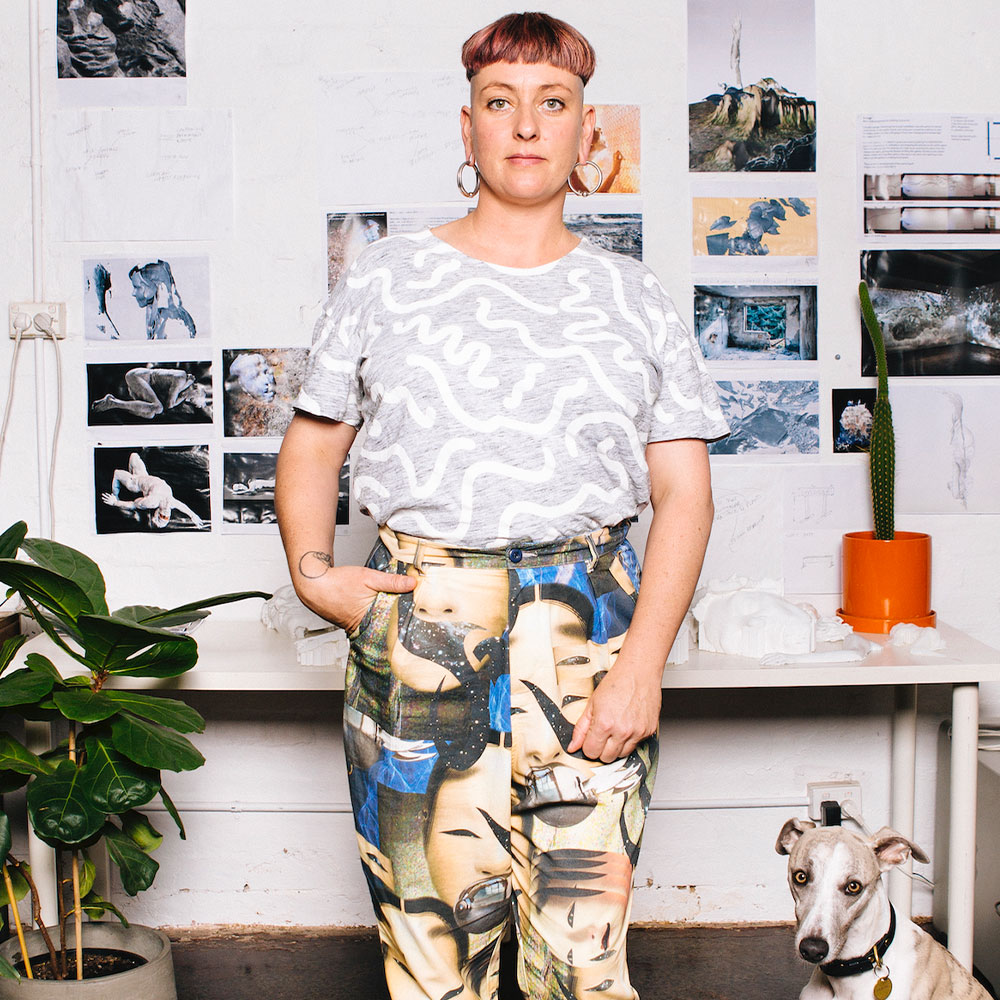 Portrait of Yandell Walton, a young woman stands facing the camera with a dog in the right had corner of the image.