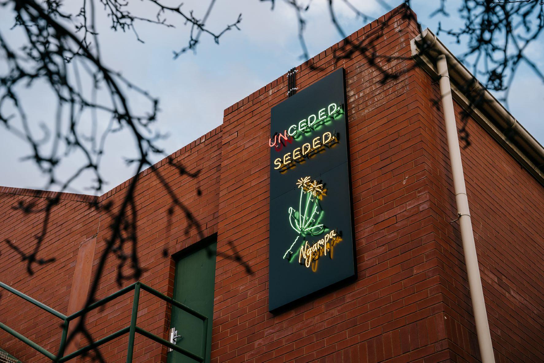 Exterior brick building with a vertical neon sign displaying 'Uncensored Seeded' and a glowing plant graphic on a dark panel.