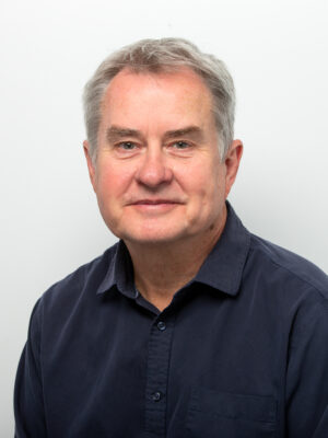 Portrait of a middle-aged man with gray hair wearing a dark blue shirt, looking at the camera.