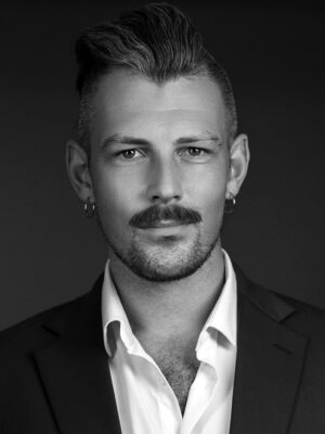 Black-and-white headshot of a man with a trimmed beard and mustache wearing a white shirt and blazer.