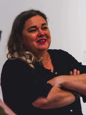 Smiling woman with arms crossed, wearing a black top, looking to the side.